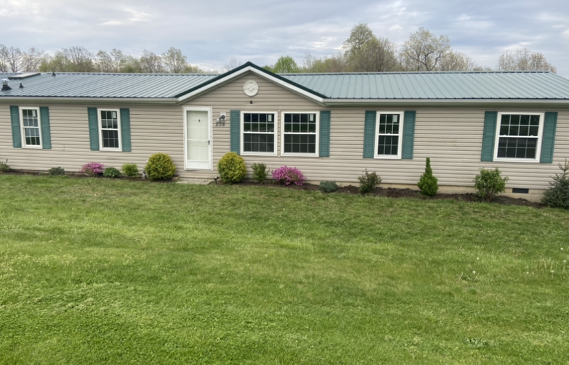 A mobile home with a green roof is sitting on top of a lush green field.