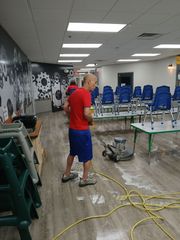 A man is cleaning the floor of a room with tables and chairs.