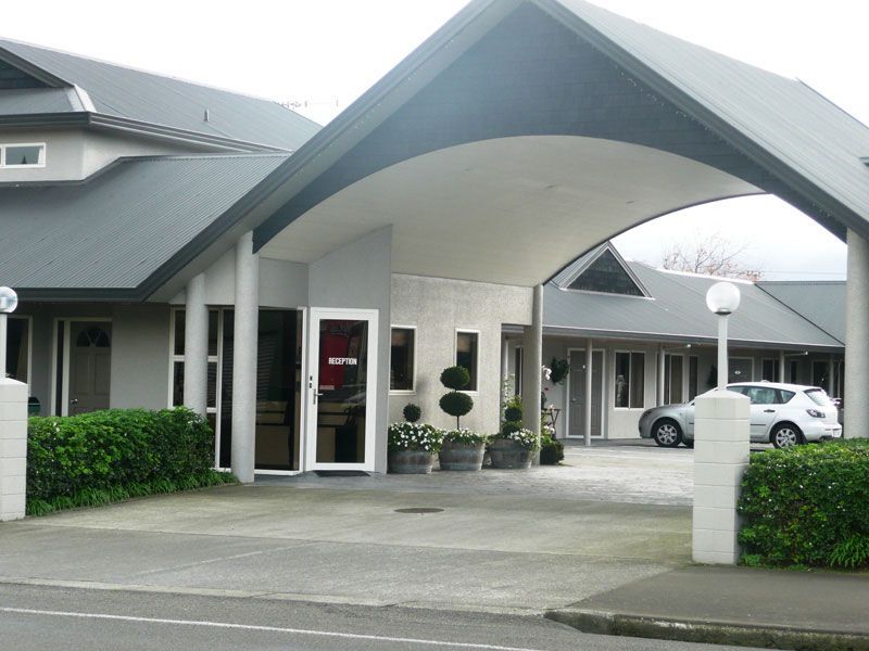Motel entrance with gray awning, columns, and parking area.