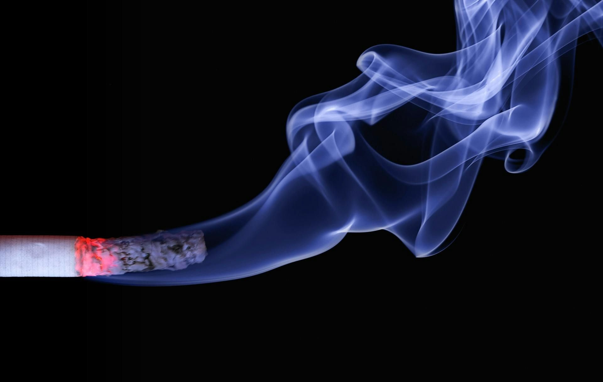 Burning cigarette emitting blue smoke against a black background.
