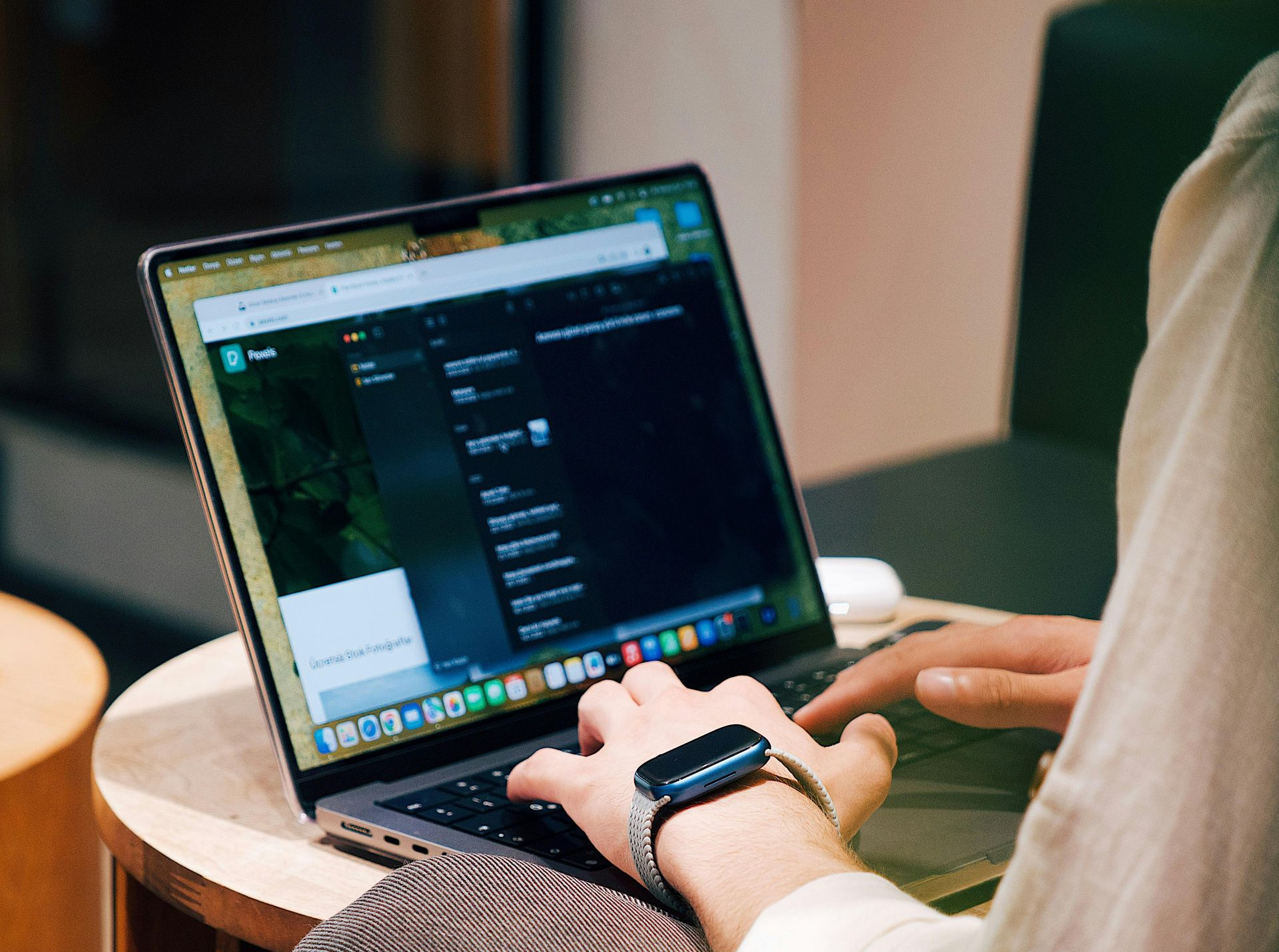 Person typing on a laptop, wearing a smartwatch. Indoor setting, neutral colors.
