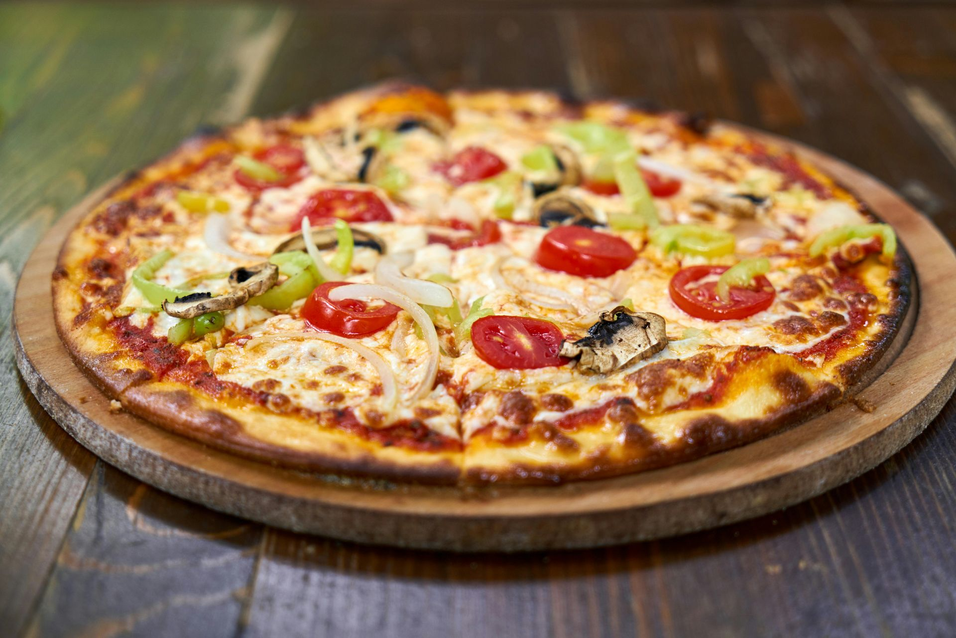 Pizza with vegetables on a wooden serving board, placed on a wooden table.