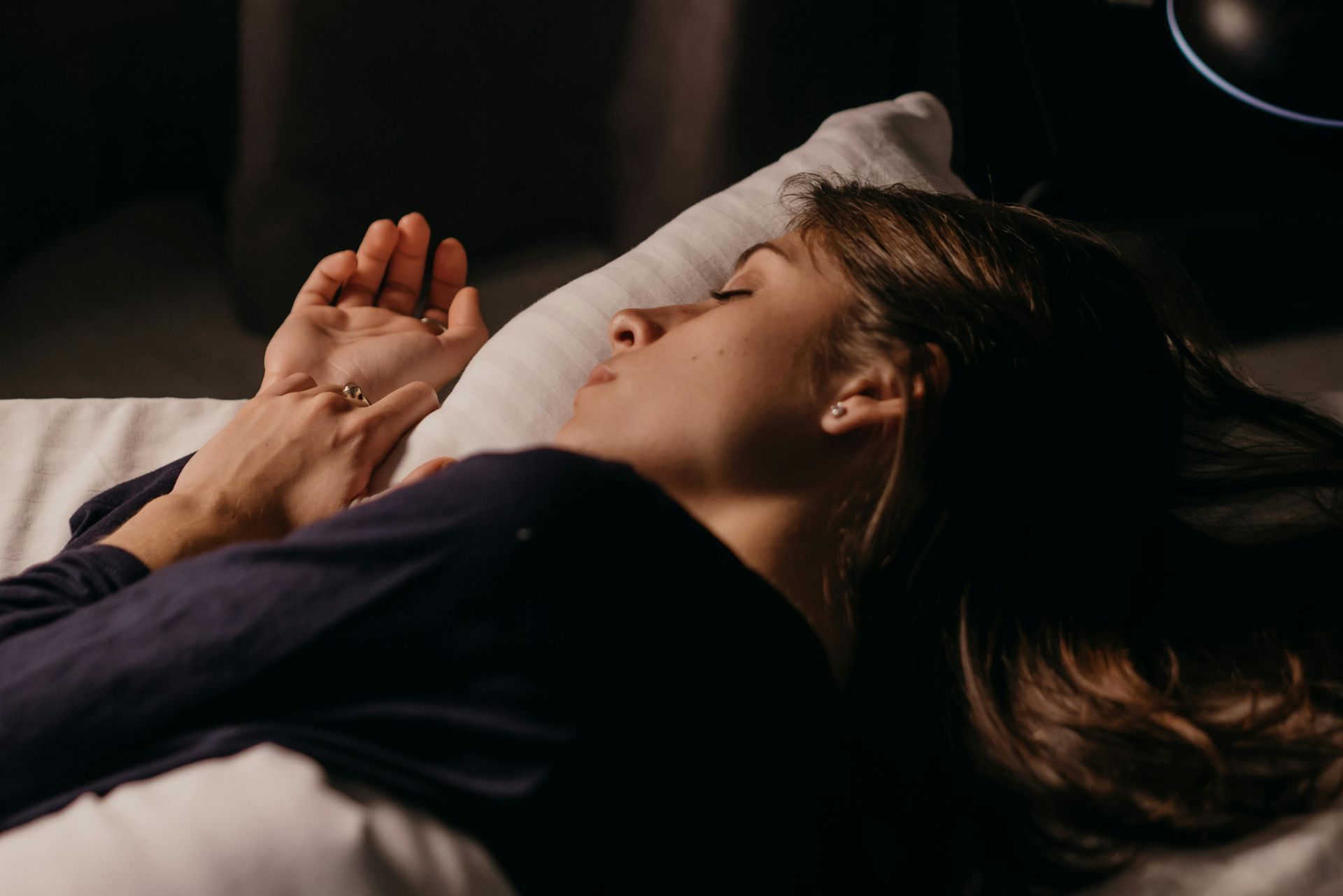 Woman asleep in bed, resting hand, wearing dark shirt, soft lighting.