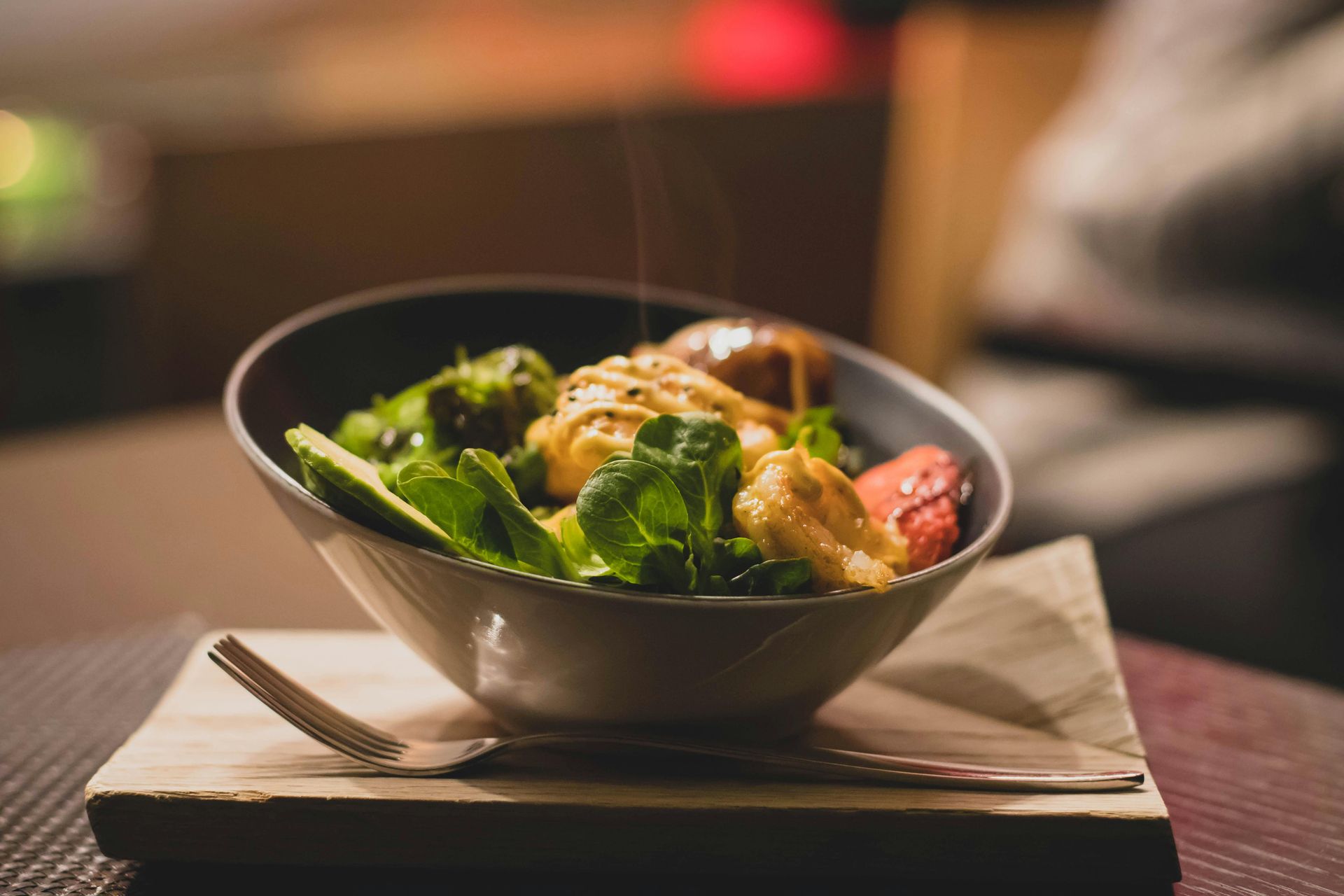 Bowl of salad with greens, strawberries, and a creamy sauce, served on a wooden board.