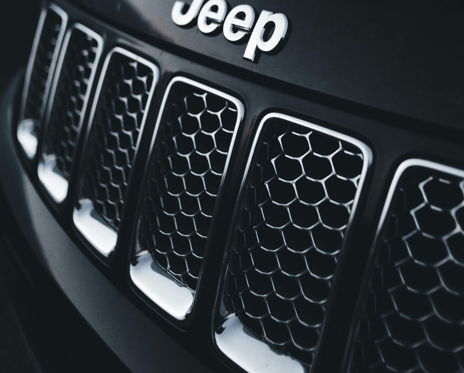 Close-up of a black Jeep grill with a chrome border and the silver "Jeep" logo at the top.