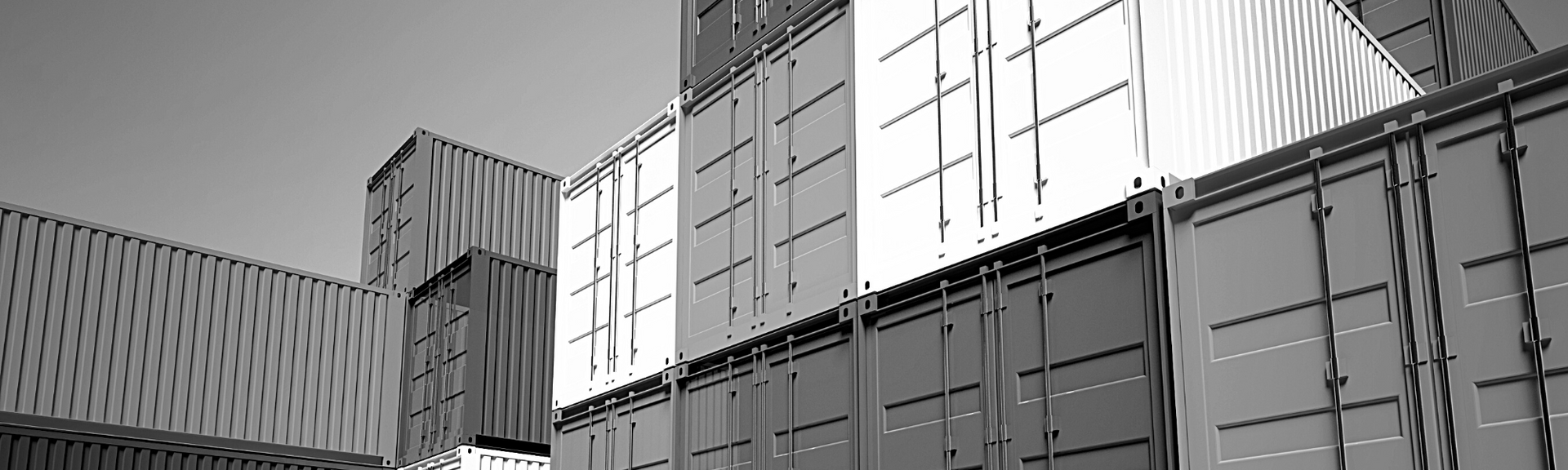 A black and white, low-angle view of stacked shipping containers in a storage yard.