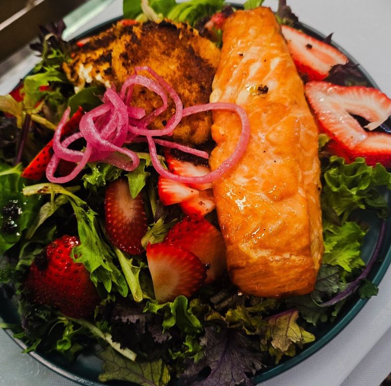A salad with salmon strawberries and onions on a plate