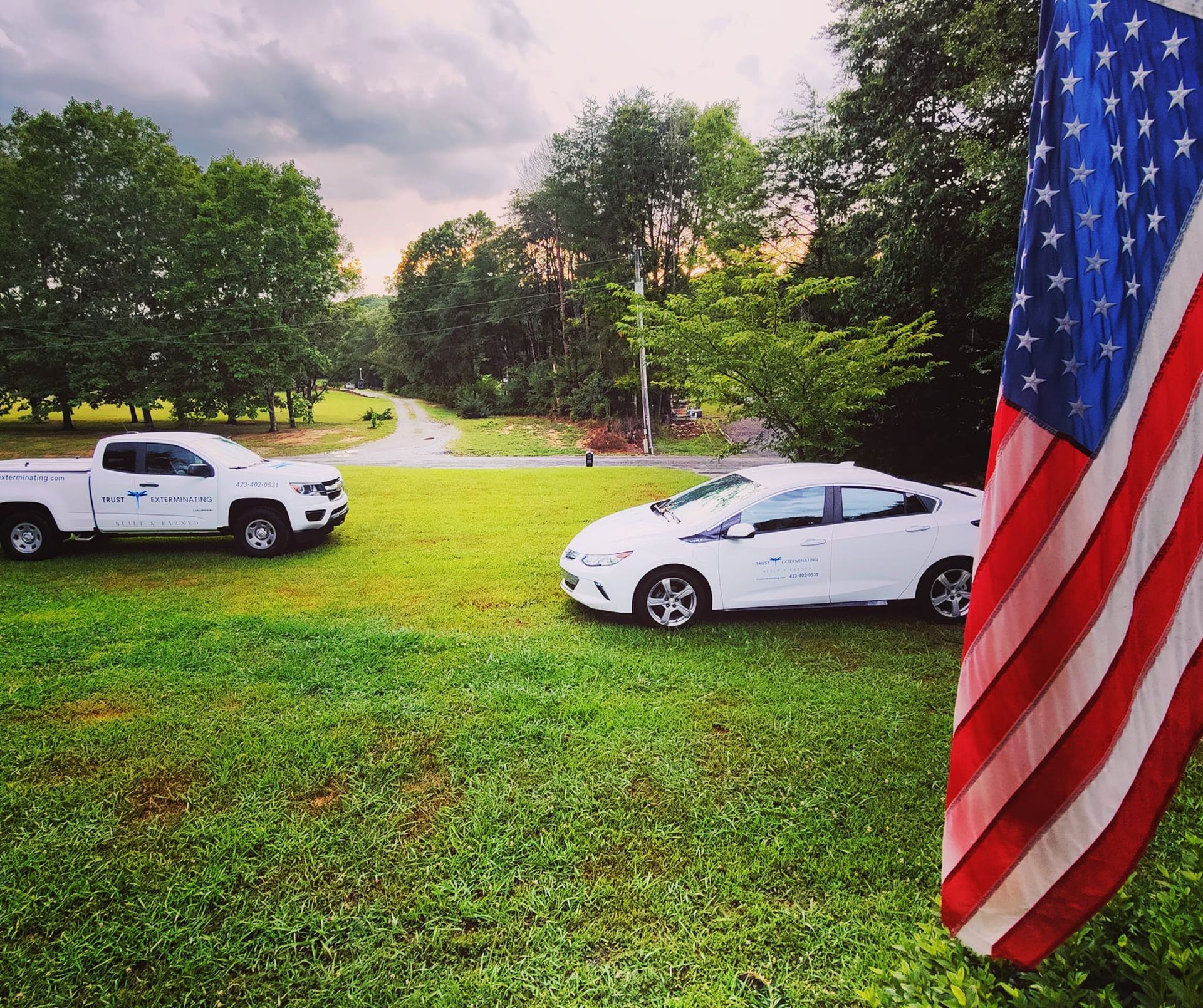 A white car is parked in a grassy field next to an american flag
