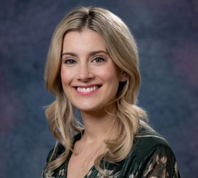 A smiling blonde woman with fair skin and light eyes poses