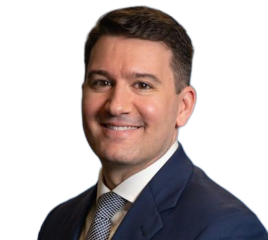 Smiling man in a navy suit and patterned tie, against a blurred blue background.