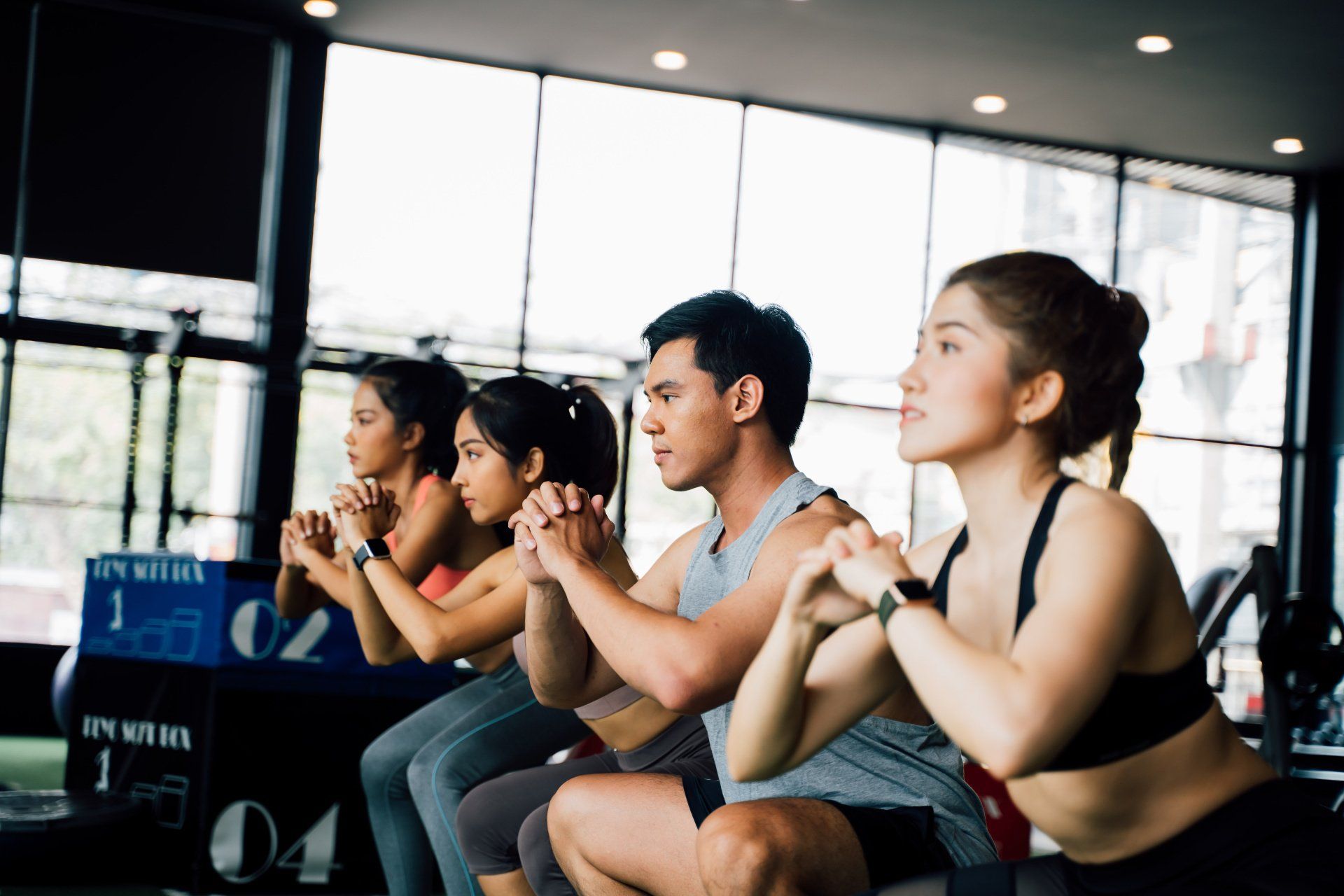 A group of people are squatting in a gym.