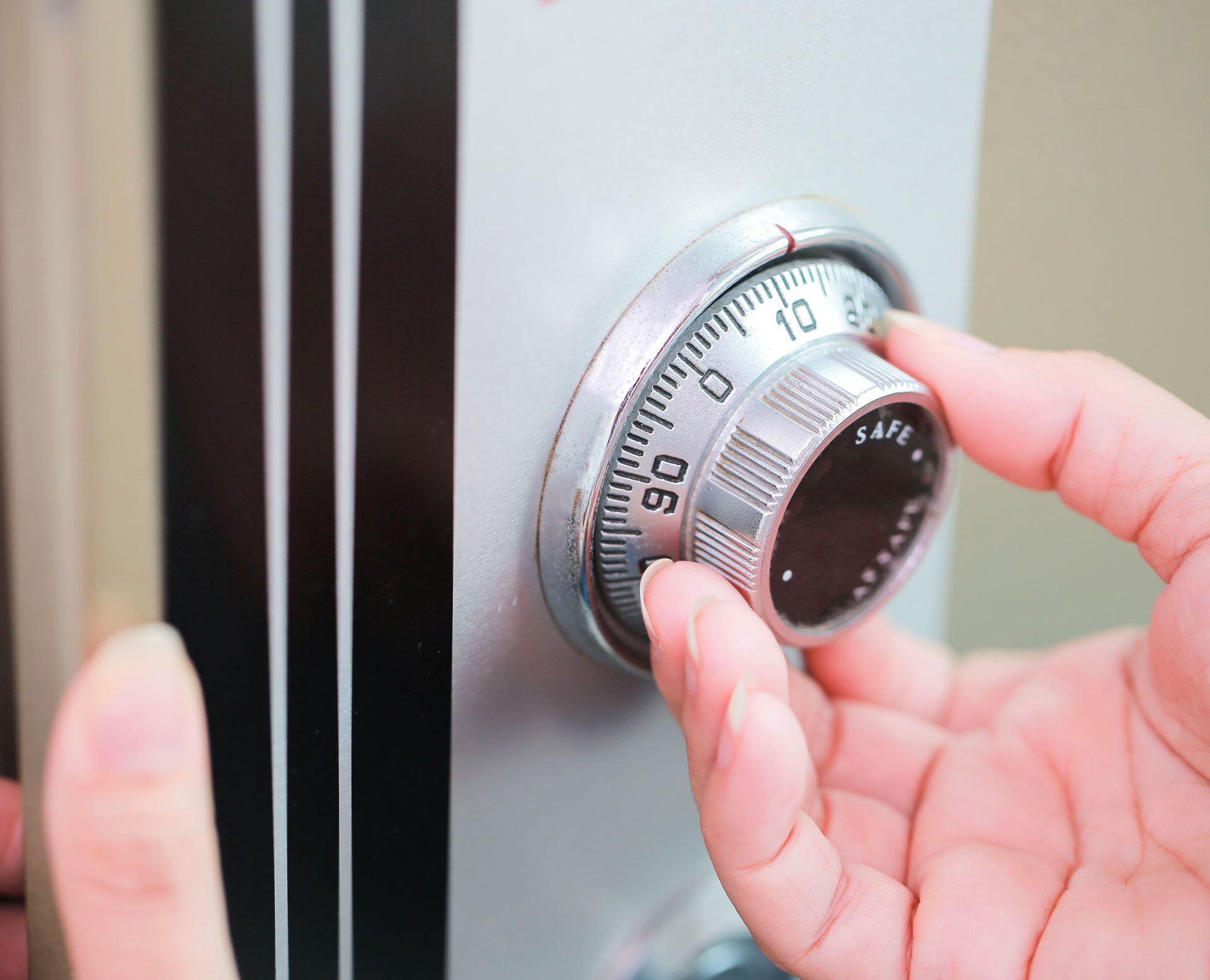 Hand turning the dial on a silver safe, the numbers visible.