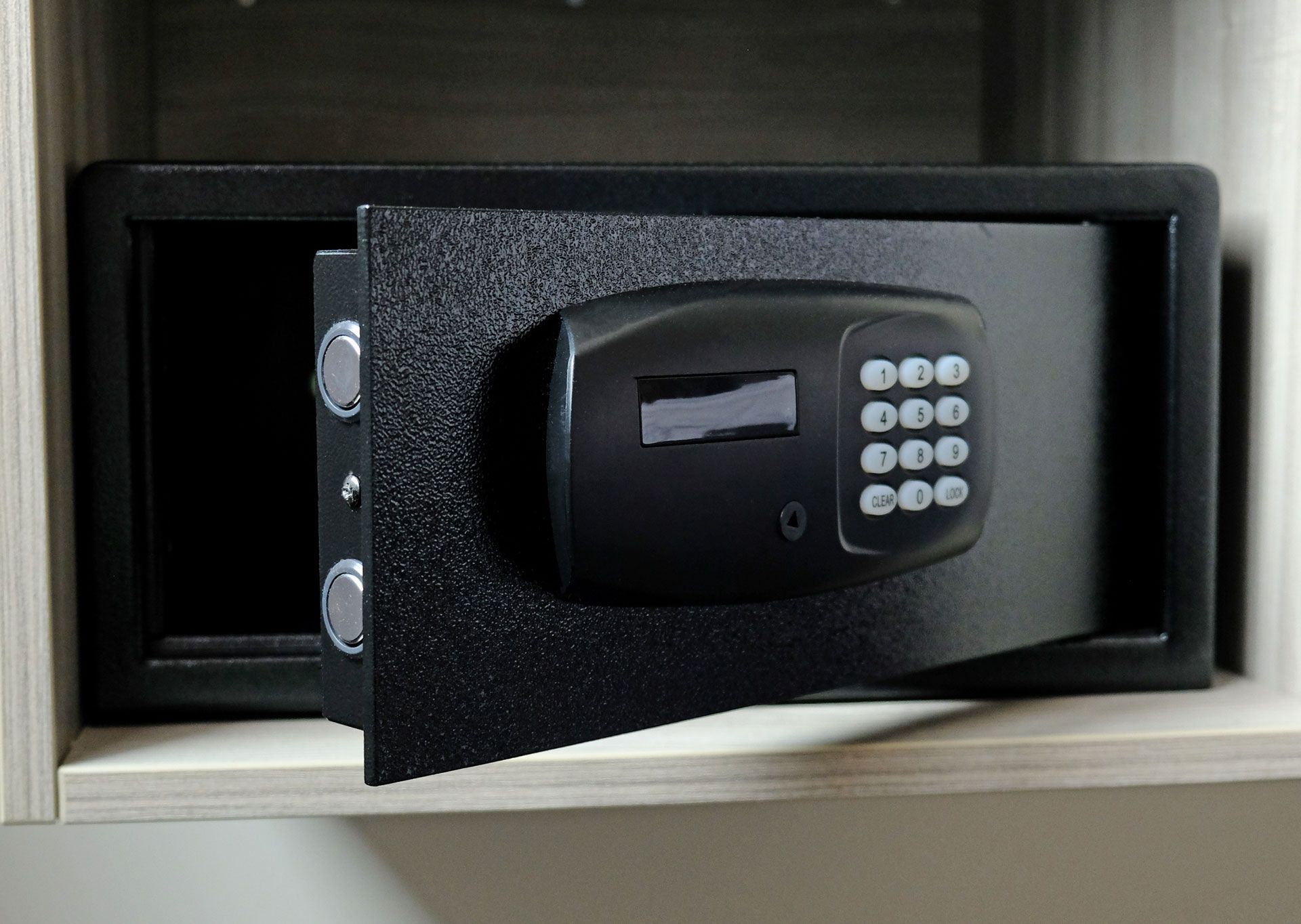 Black digital safe with open door, mounted in a light-colored cabinet.