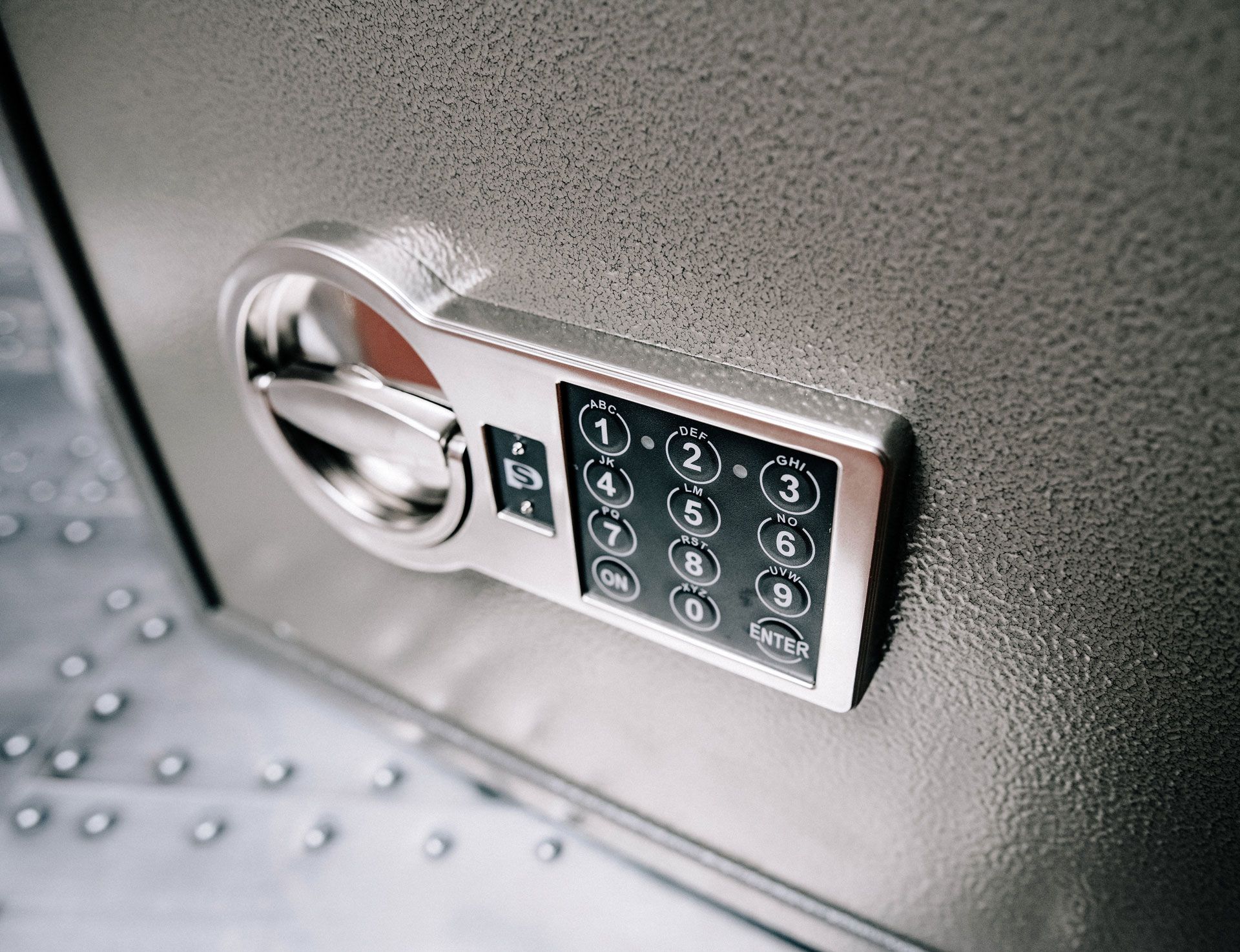 Close-up of a silver safe's keypad and dial on a textured gray surface.