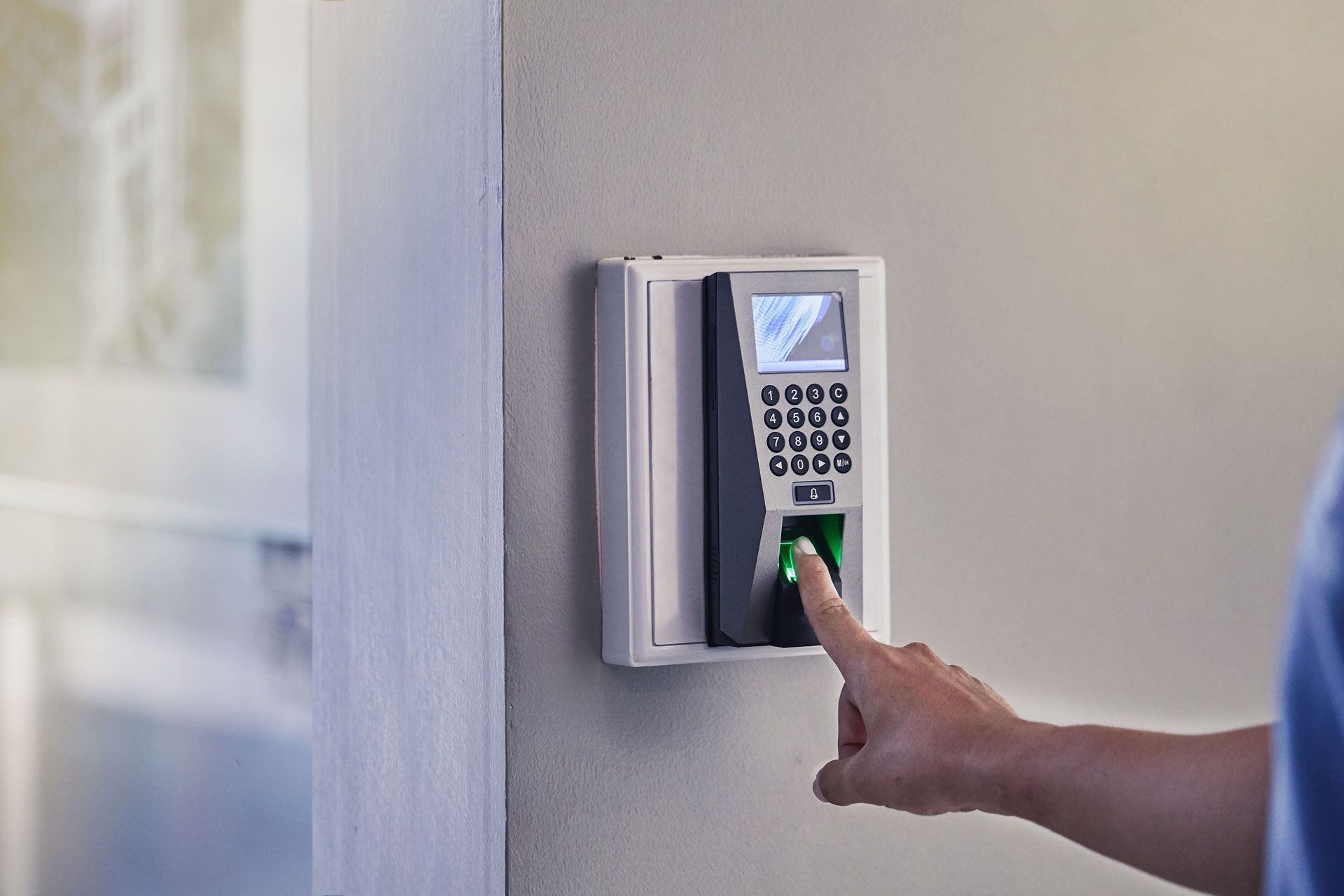 Person using fingerprint scanner on a wall-mounted security device.