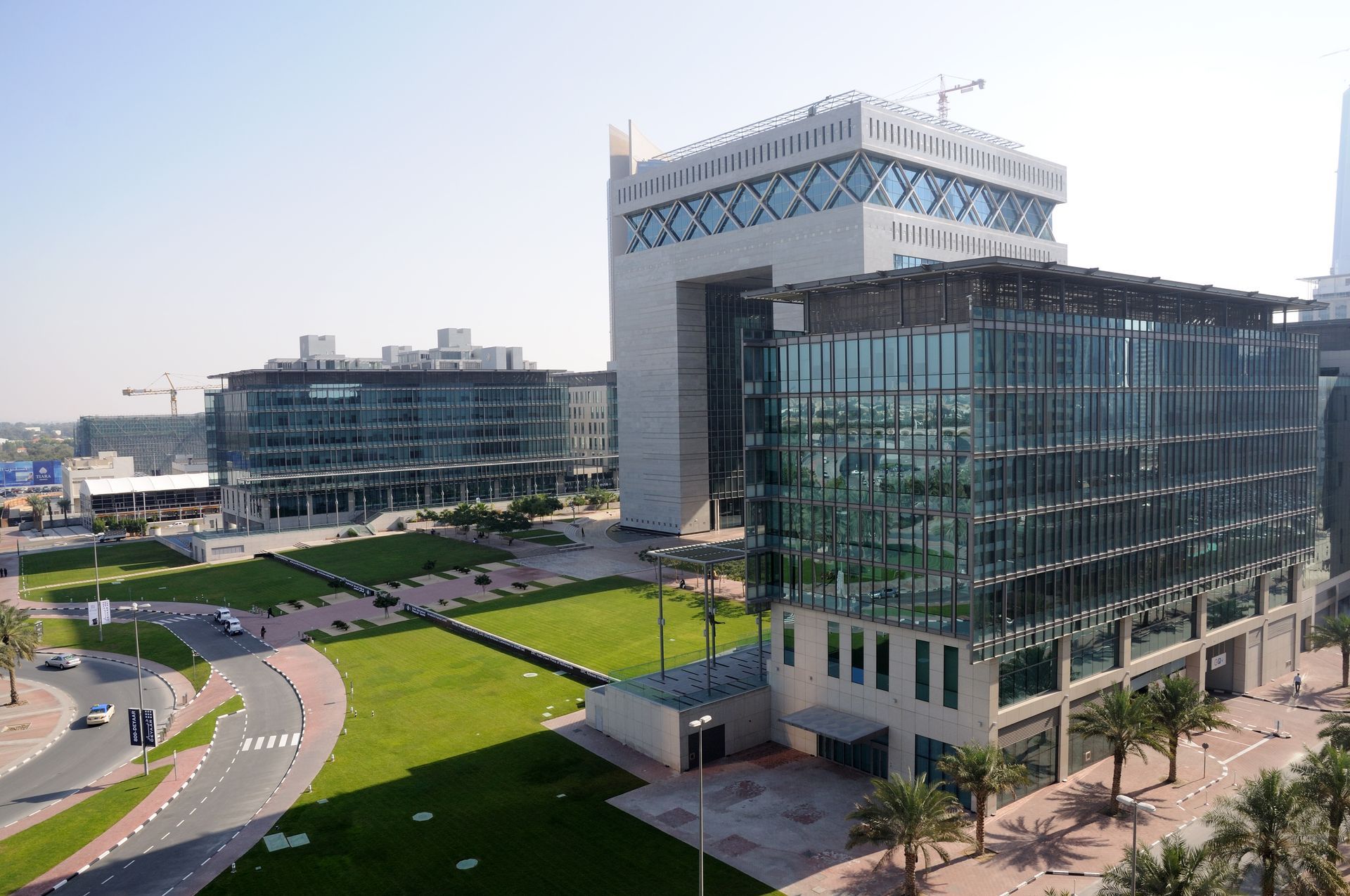 Modern glass office buildings beside a green lawn and curved road on a sunny day