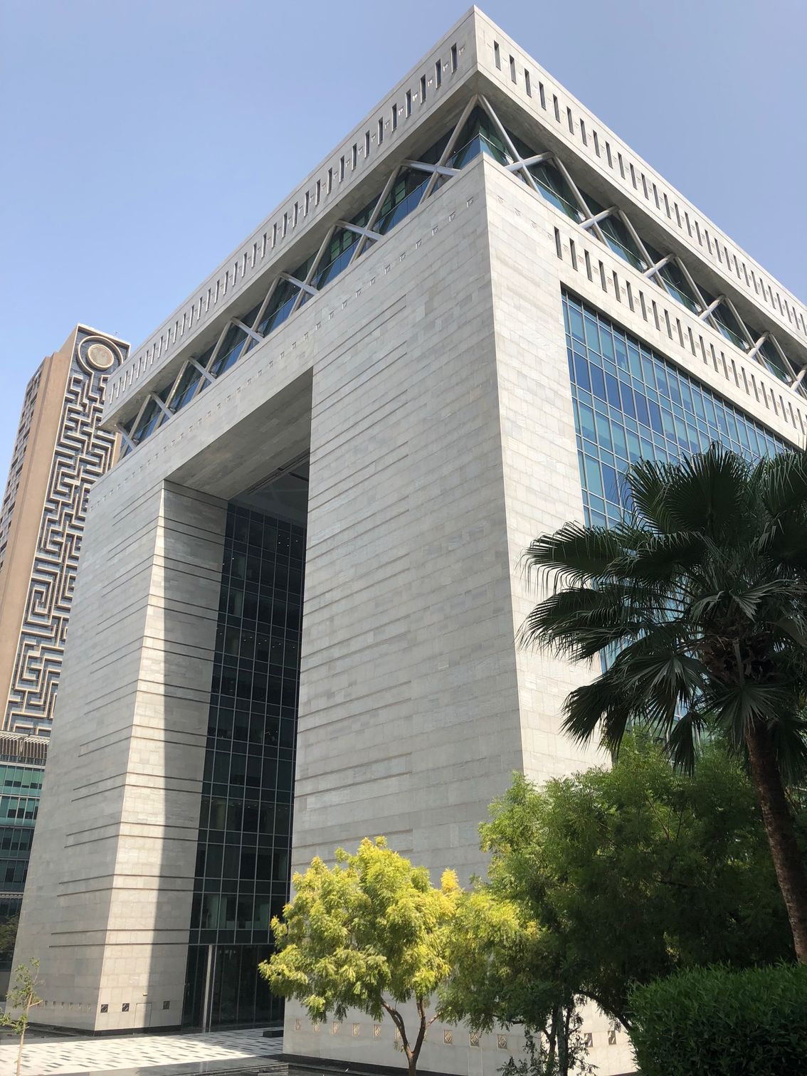 Tall modern office building with a large archway, blue glass, and trees in front under a clear sky