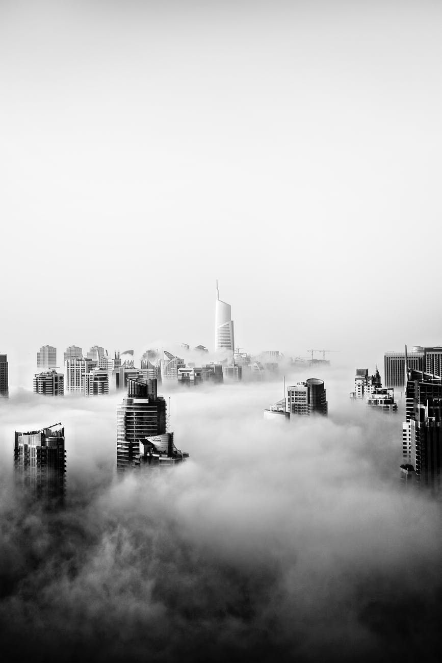 Black-and-white city skyline rising above dense fog, with a tall central skyscraper in the distance