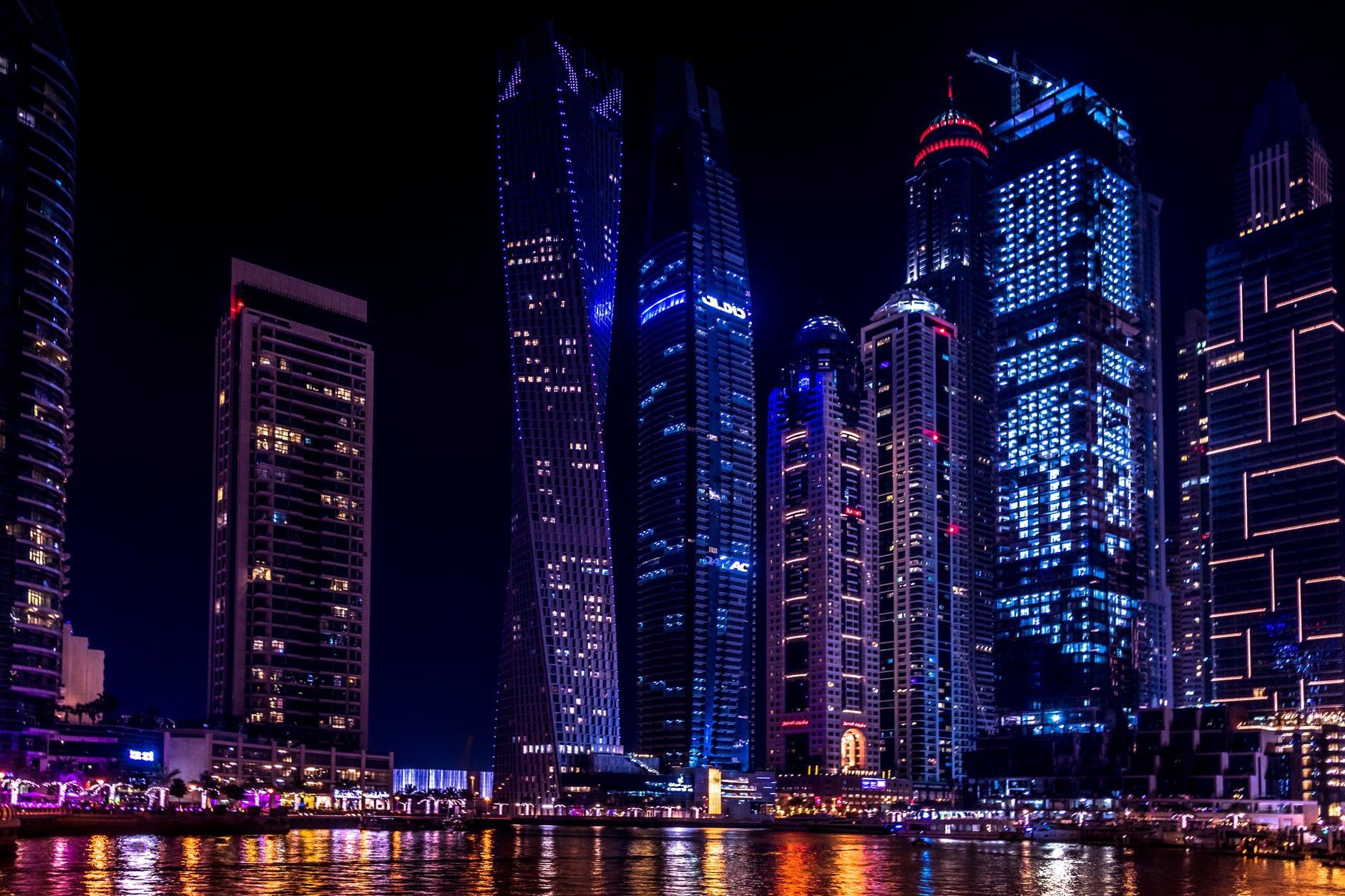 Neon-lit city skyline at night with towering blue and purple skyscrapers reflected on water