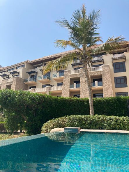 Resort pool with turquoise water, palm tree, and beige apartment building under a clear blue sky