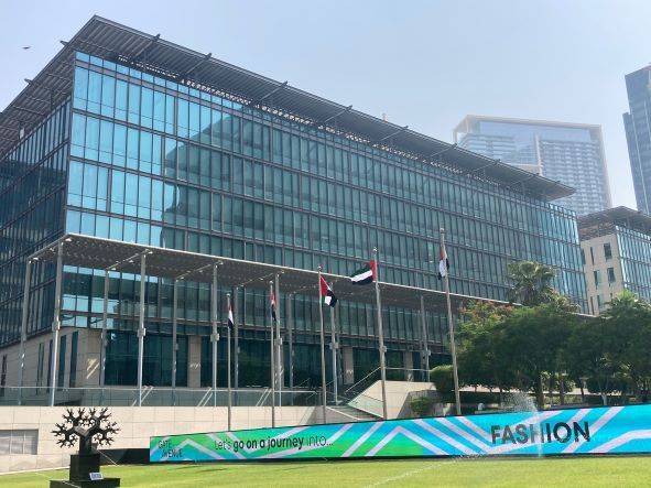 Modern glass office building with Canadian flags and a green “FASHION” banner out front
