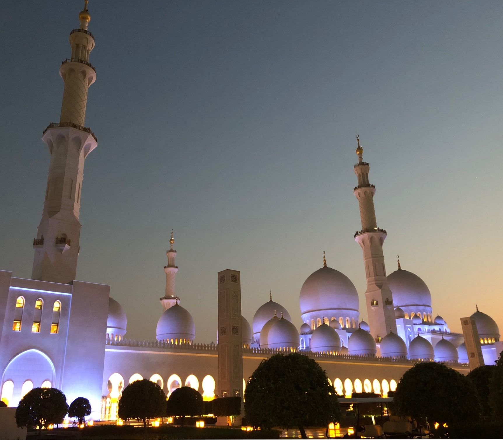 Illuminated mosque with domes and tall minarets at dusk under a clear sky