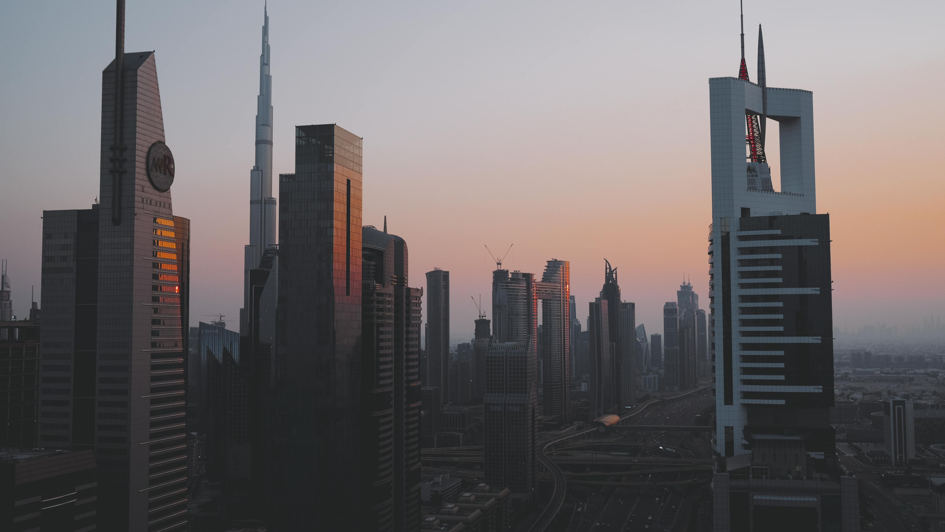 City skyline at dusk with modern skyscrapers and a pink-orange sunset sky