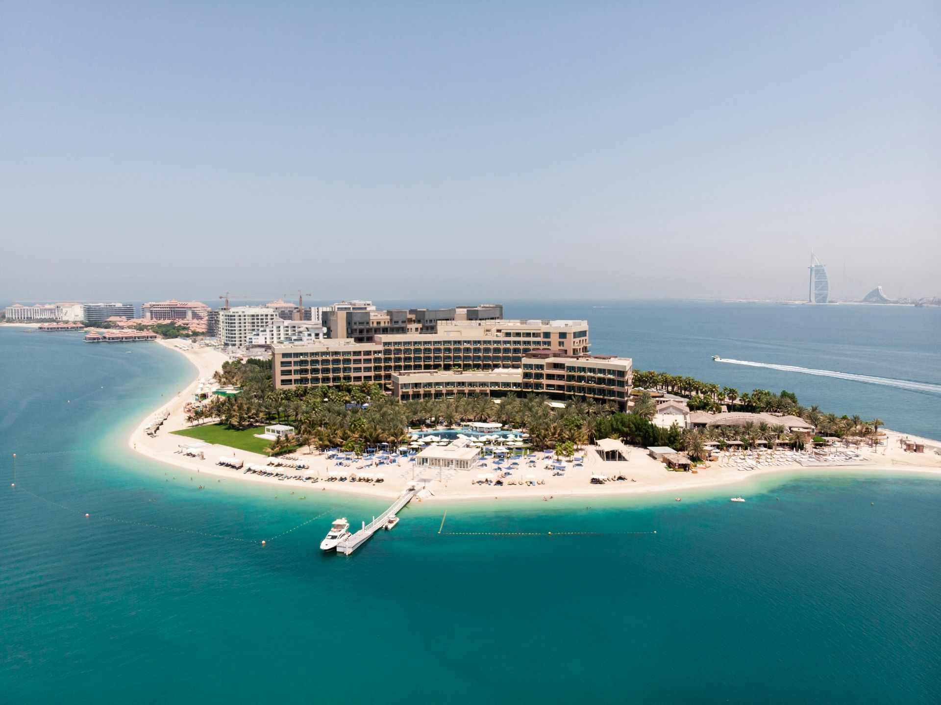 Aerial view of a tropical resort on a small island, surrounded by turquoise water and a sandy beach.