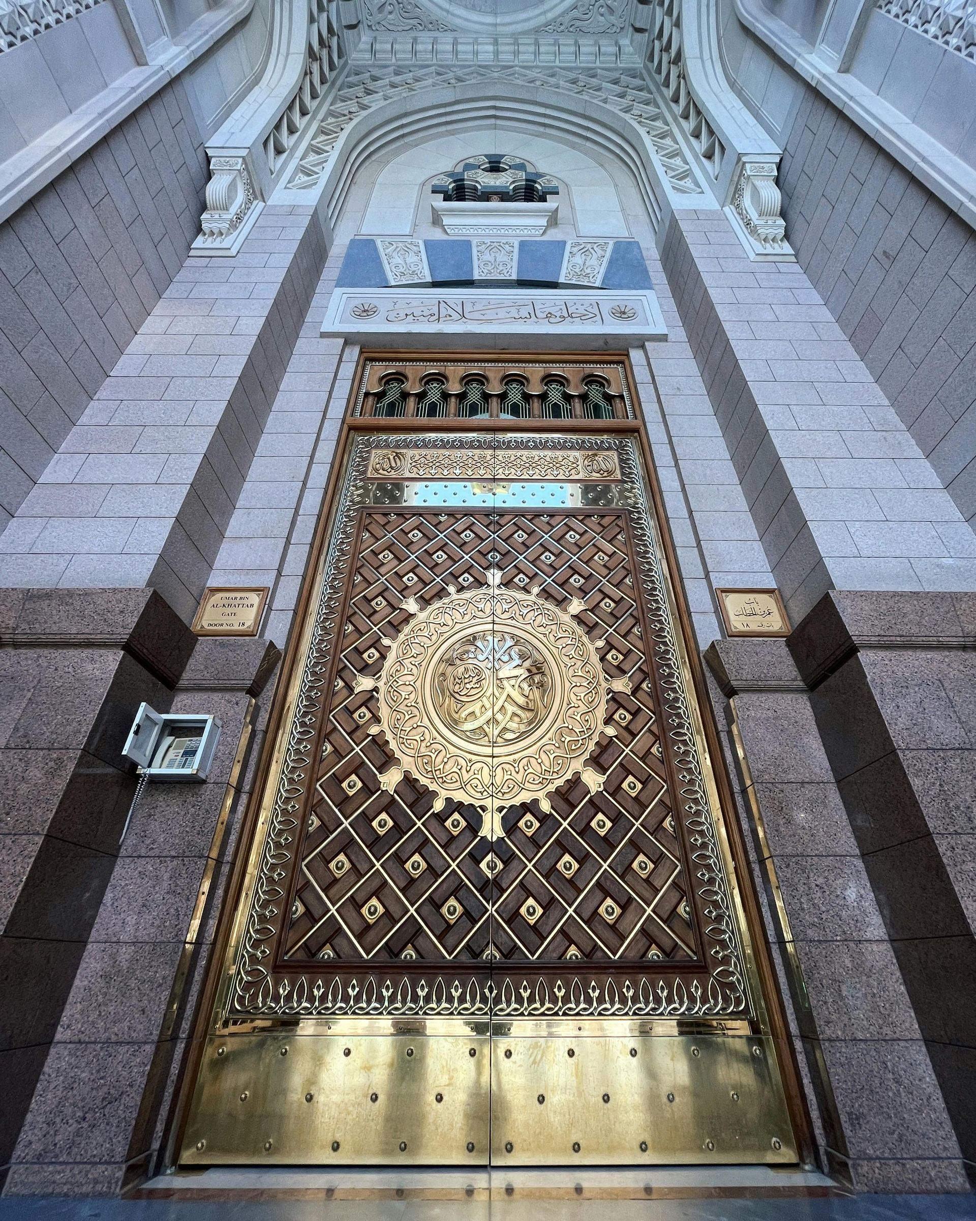 Ornate golden mosque door with Arabic calligraphy beneath an arched stone facade