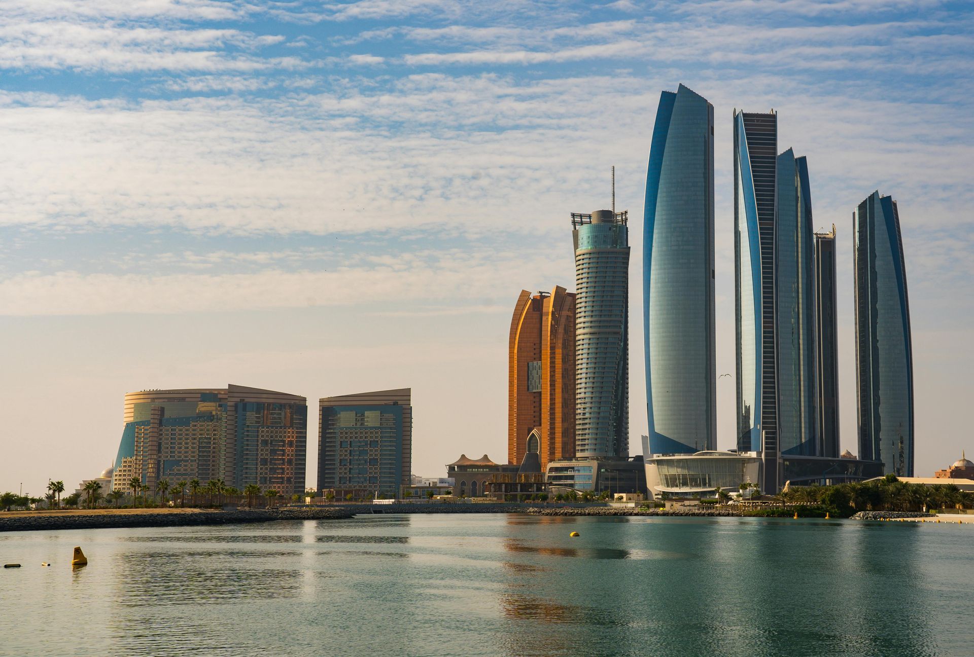 Modern waterfront skyline with glass skyscrapers and low buildings reflected in calm water at sunset