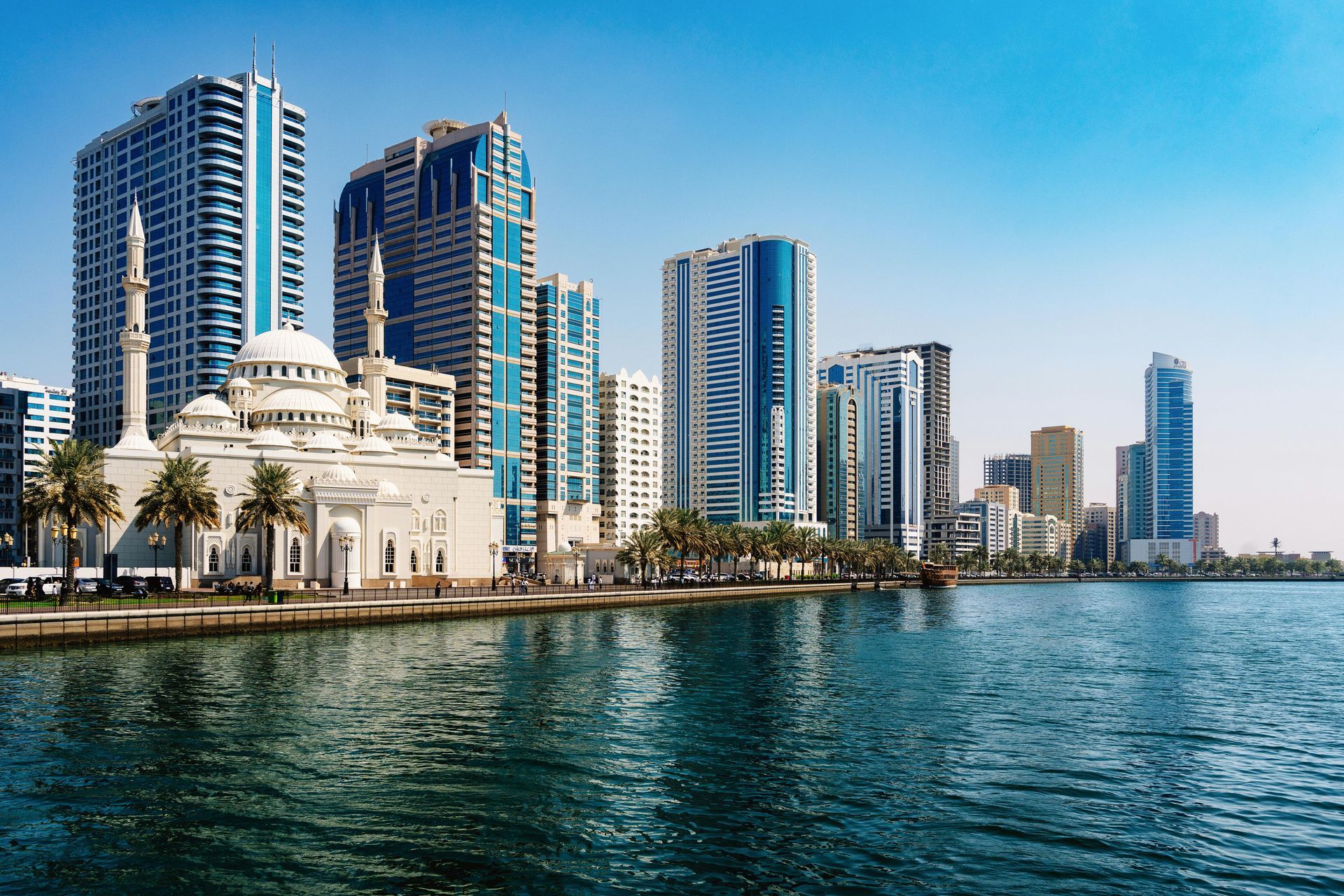 Modern waterfront skyline with tall glass towers beside calm blue water under a clear sky