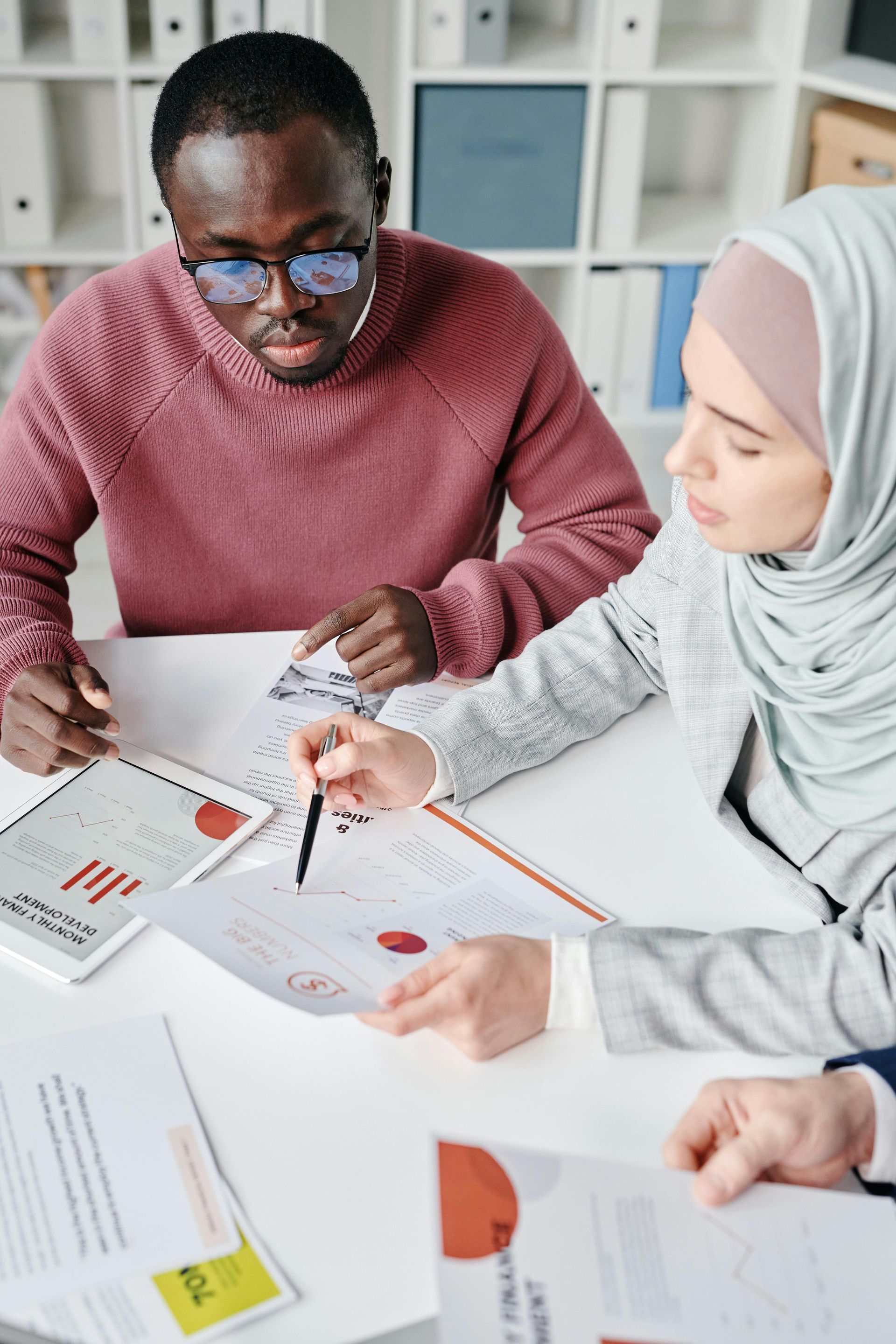 Two coworkers reviewing printed charts and notes at a desk in a bright office