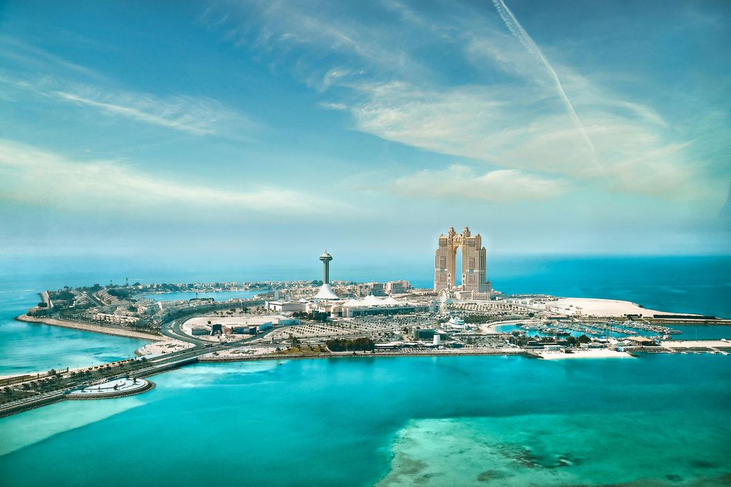 Aerial view of a turquoise island with modern towers, a waterfront skyline, and a tall observation tower