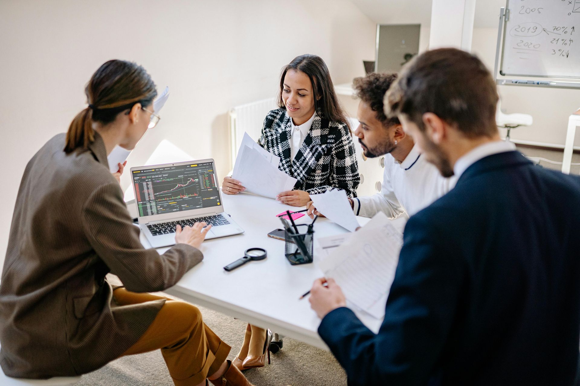 Four people in a meeting around a table, reviewing papers and a laptop in a bright office.