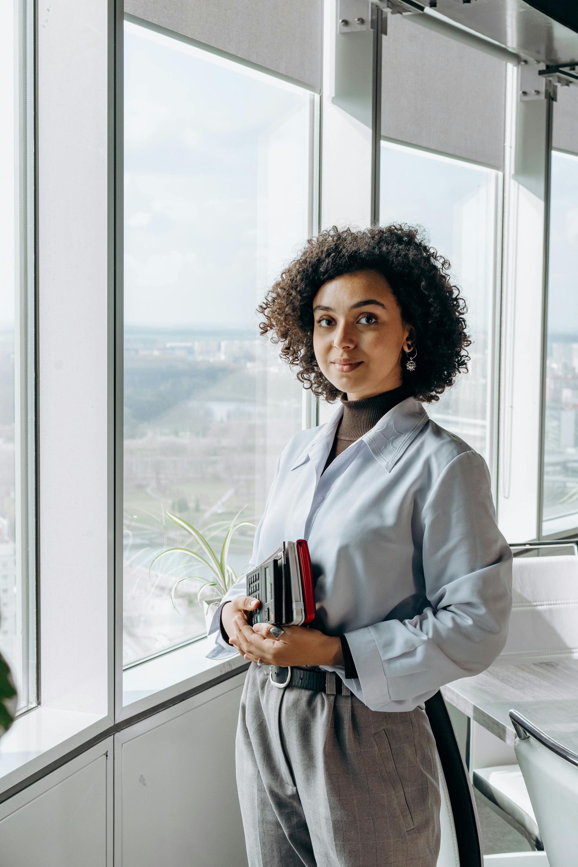 Woman holding books in a bright office by floor-to-ceiling windows