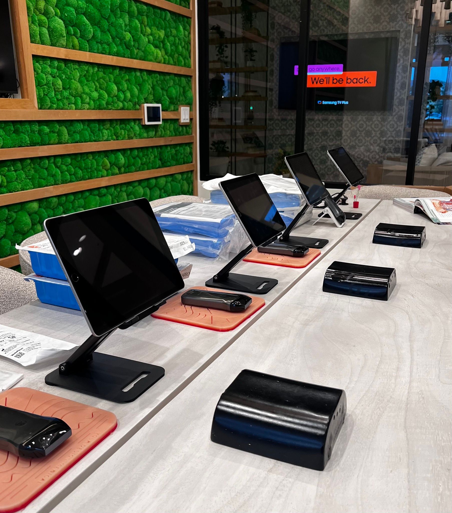 A row of computer monitors are sitting on a table in front of a wall with moss growing on it.