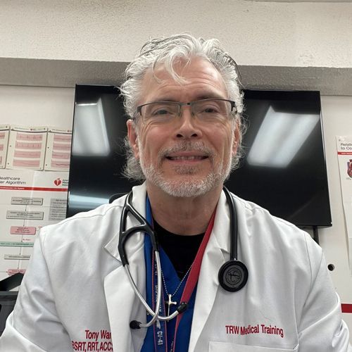 Man in white coat with stethoscope, smiling. TRW Medical Training in background.