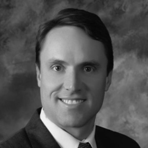 Man in a suit smiles at the camera, headshot in black and white.
