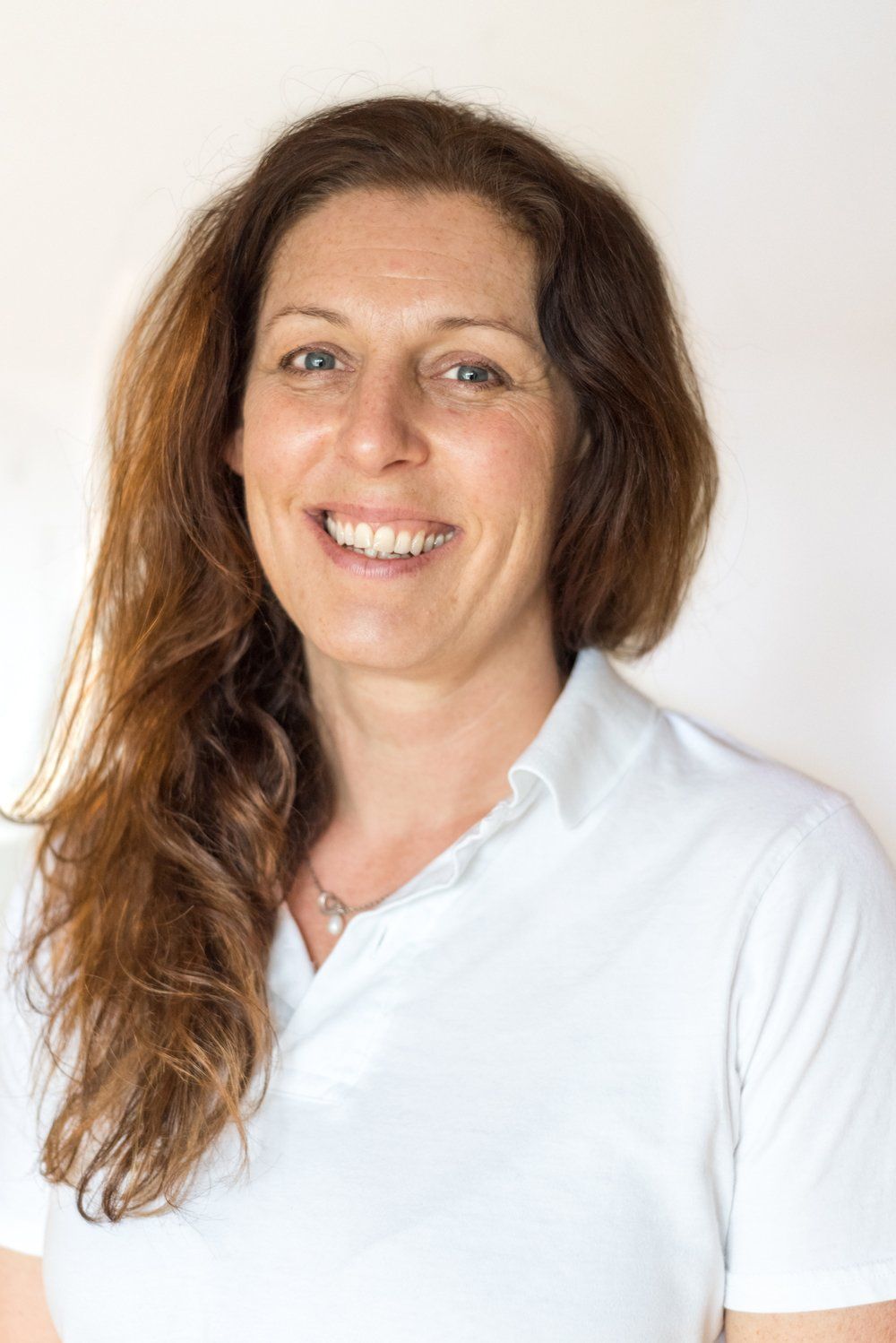 Eine Frau mit langen Haaren trägt ein weisses Hemd und lächelt.