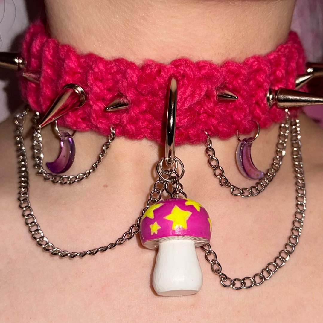 A woman wearing a pink choker with spikes and a mushroom pendant