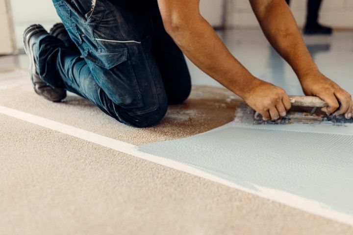 A man is kneeling on the floor using a trowel.