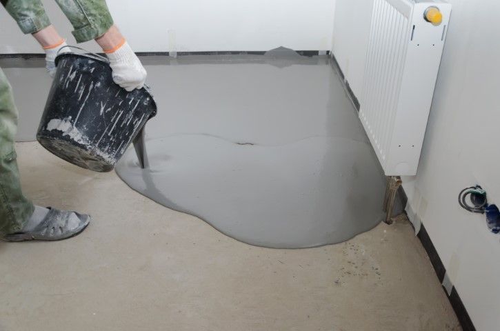 A person is pouring concrete into a room with a bucket.