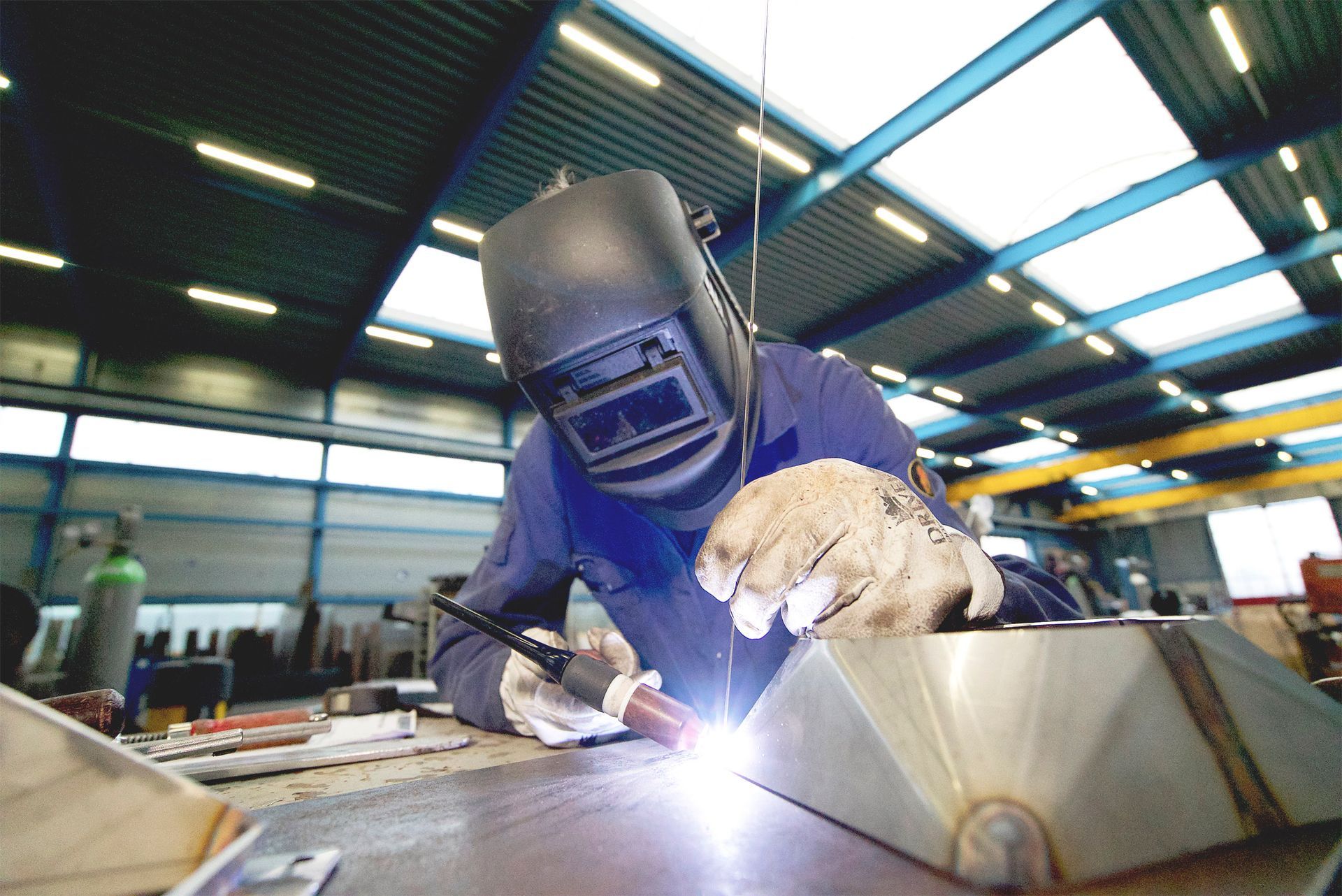 A man wearing a welding mask is welding a piece of metal