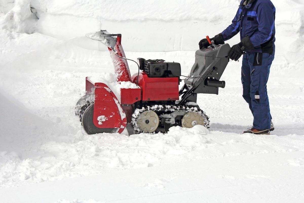 Man operating a snowblower to clear heavy snow from a snowy road during winter.