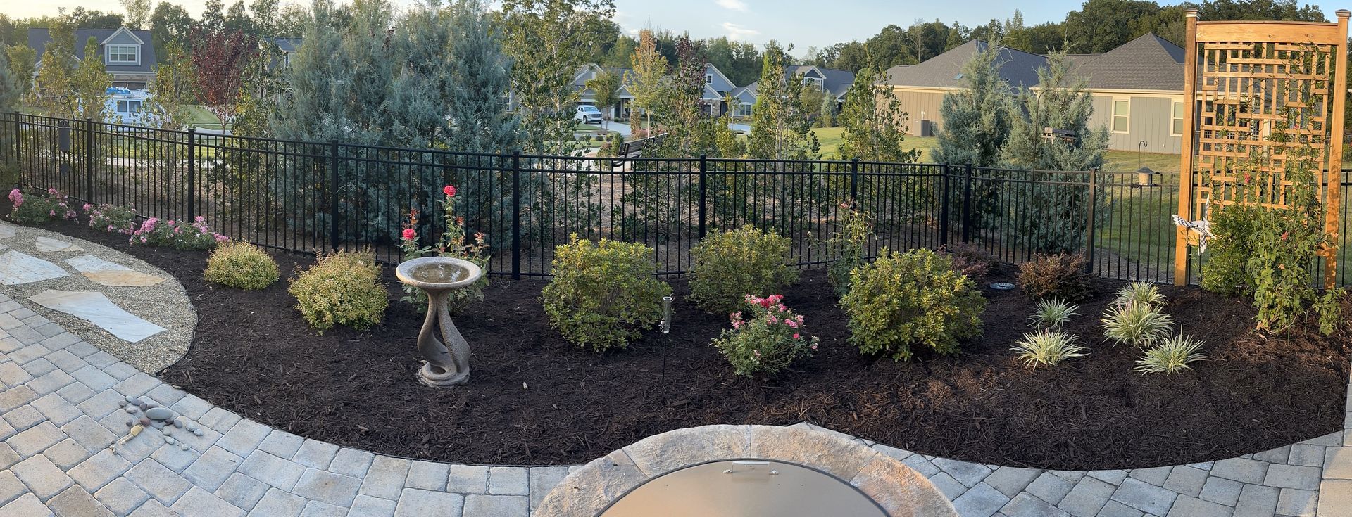 Backyard with brick patio, black fence, flowerbeds, and a birdbath.