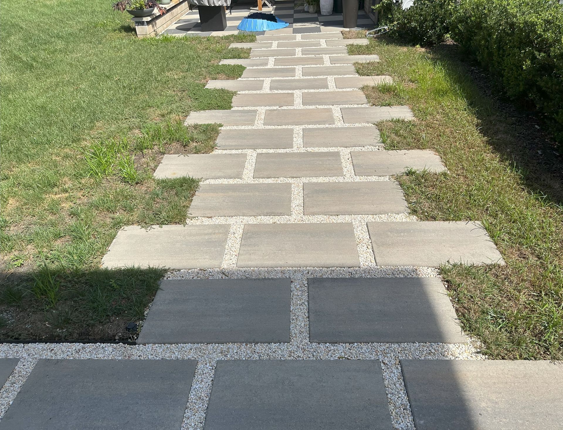 Gray stone pavers create a pathway through a grassy yard, interspersed with white gravel.