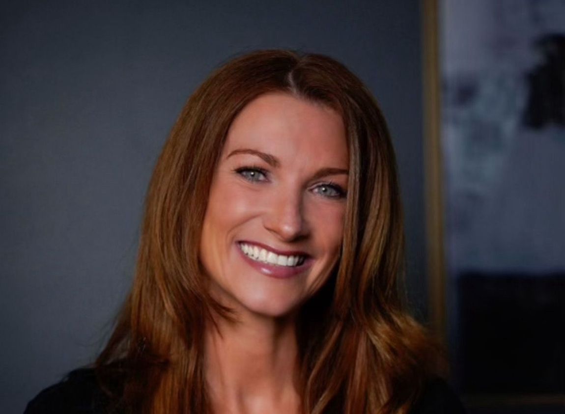 A woman with long red hair is smiling for the camera