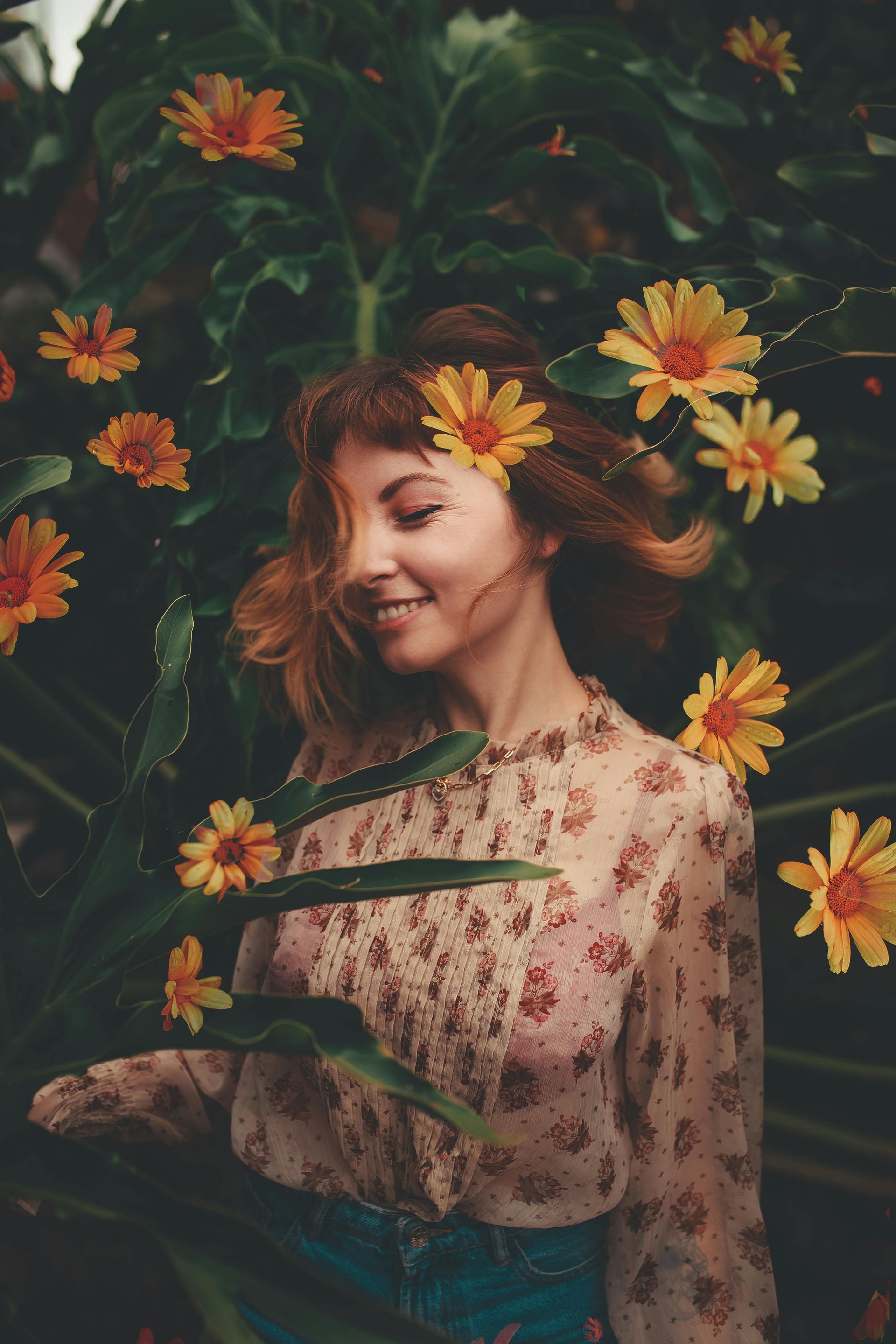 A woman with flowers in her hair is standing in a field of flowers.