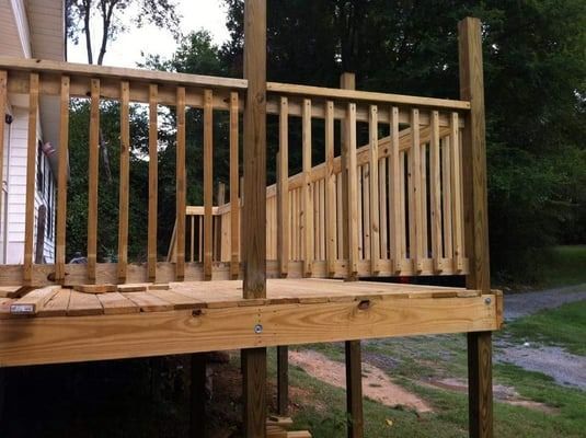 A wooden deck with a railing is sitting in front of a house.