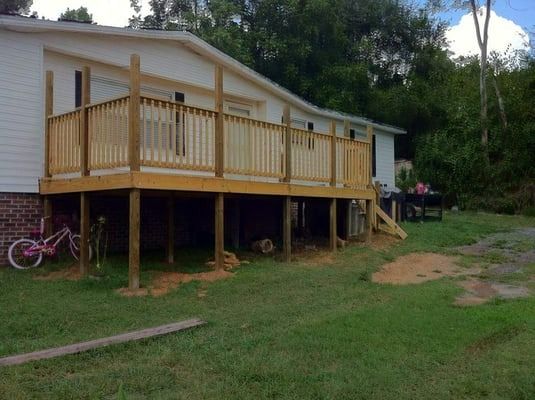 A mobile home with a large wooden deck and a pink bike parked in front of it.